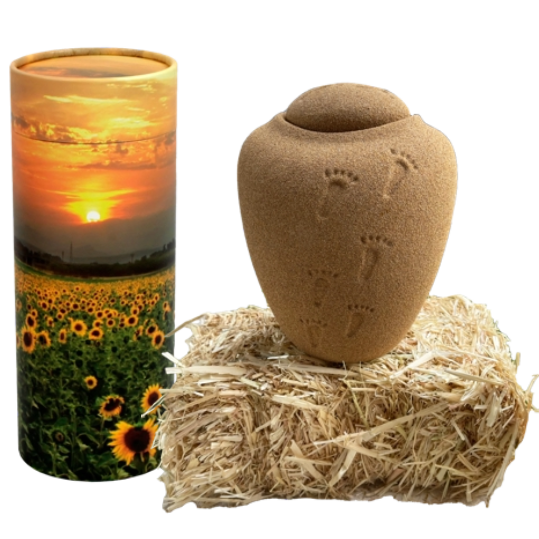 Biodegradable urn options including a cylindrical urn with a sunflower field and sunset design and a sand-colored urn with footprint details resting on a bale of straw.